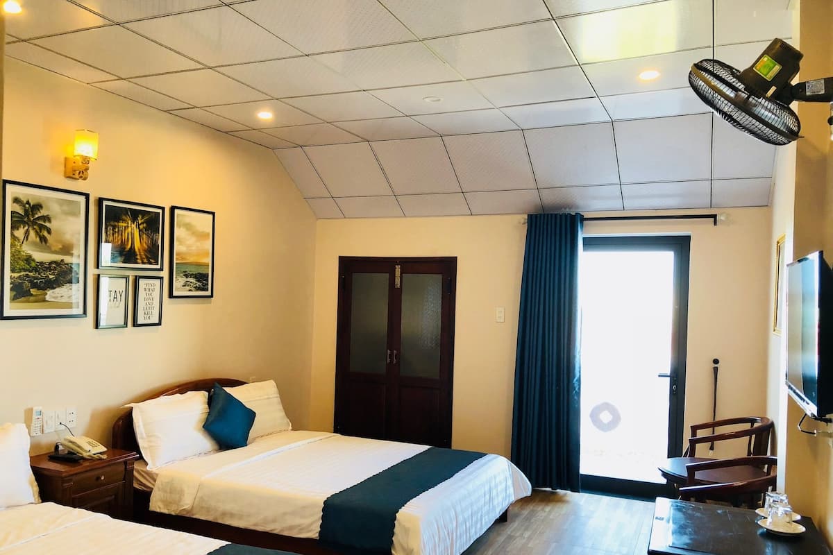A hotel room with two beds, a desk, a TV, and a window with curtains.