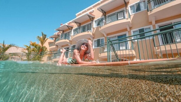 A swimming pool with clear water, a person lying on the edge, and a building with balconies in the background. - Il Palazzo Boutique Apartment Hotel (Cairns)