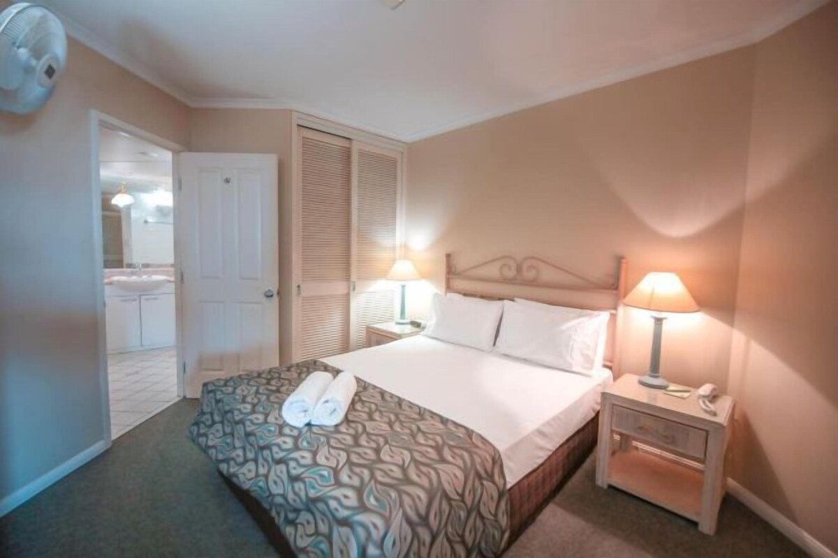 Habitación de hotel con cama, lámparas de noche, mesita de noche y puerta que da a un baño.