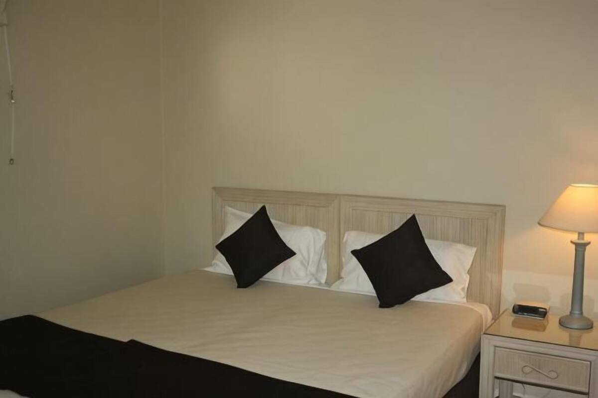 Ein Bett mit weißen Bettwäsche und schwarzen Kissen, ein Nachttisch mit Lampe und ein Beistelltisch mit Telefon.
