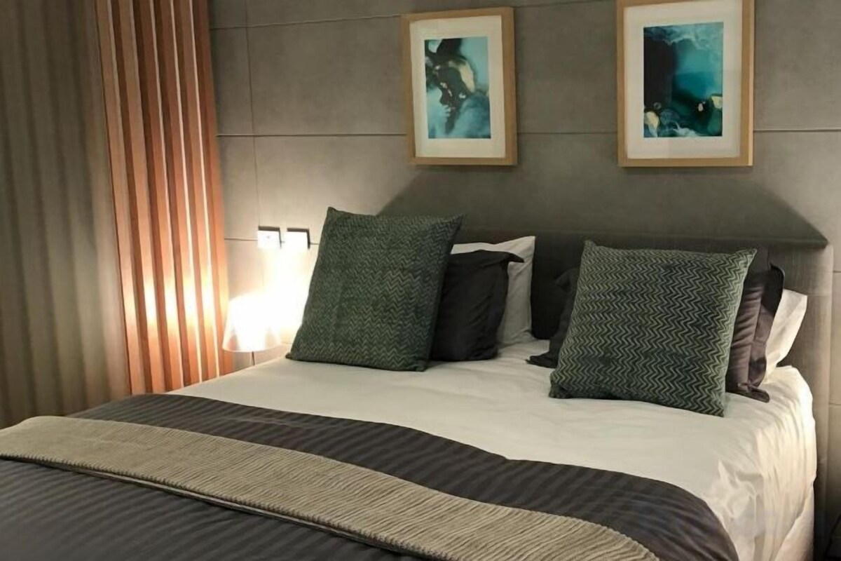 Une chambre d’hôtel avec un lit, deux oreillers, une tête de lit et deux tableaux encadrés accrochés au mur.