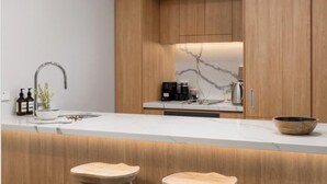 A modern kitchen with wooden cabinets, a marble backsplash, a stainless steel sink, and two wooden stools. - Il Palazzo Boutique Apartment Hotel (Cairns)