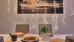 Ein Esstisch ist gedeckt mit Tellern, Schüsseln und einem Blumentopf. An der Wand hängt ein gerahmtes Bild von einem Boot.