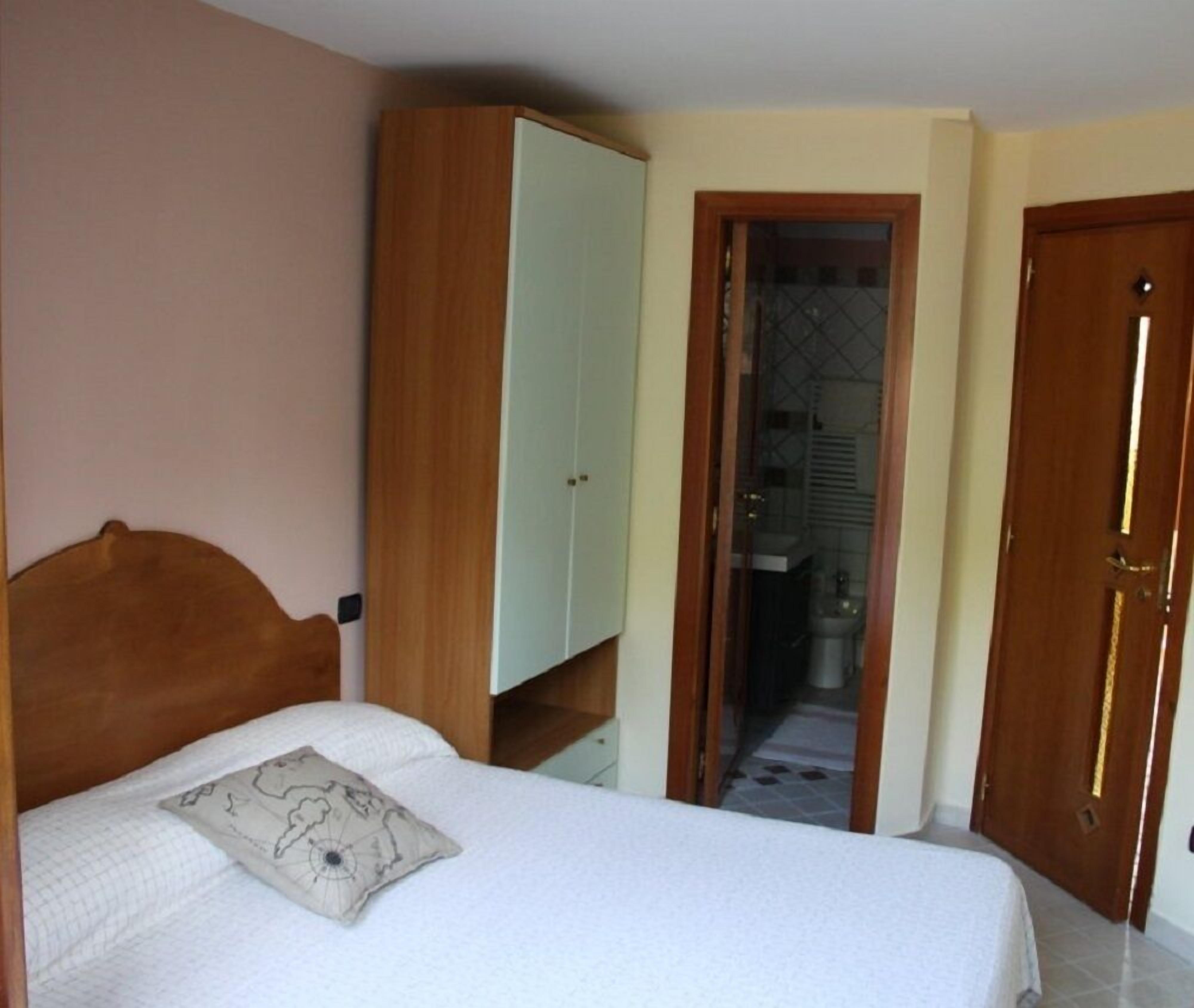 Un dormitorio con cama, armario y baño visible a través de una puerta abierta.