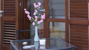 Une table en verre ornée d’un vase de fleurs roses et d’une bougie, placée devant une porte en bois munie de volets.