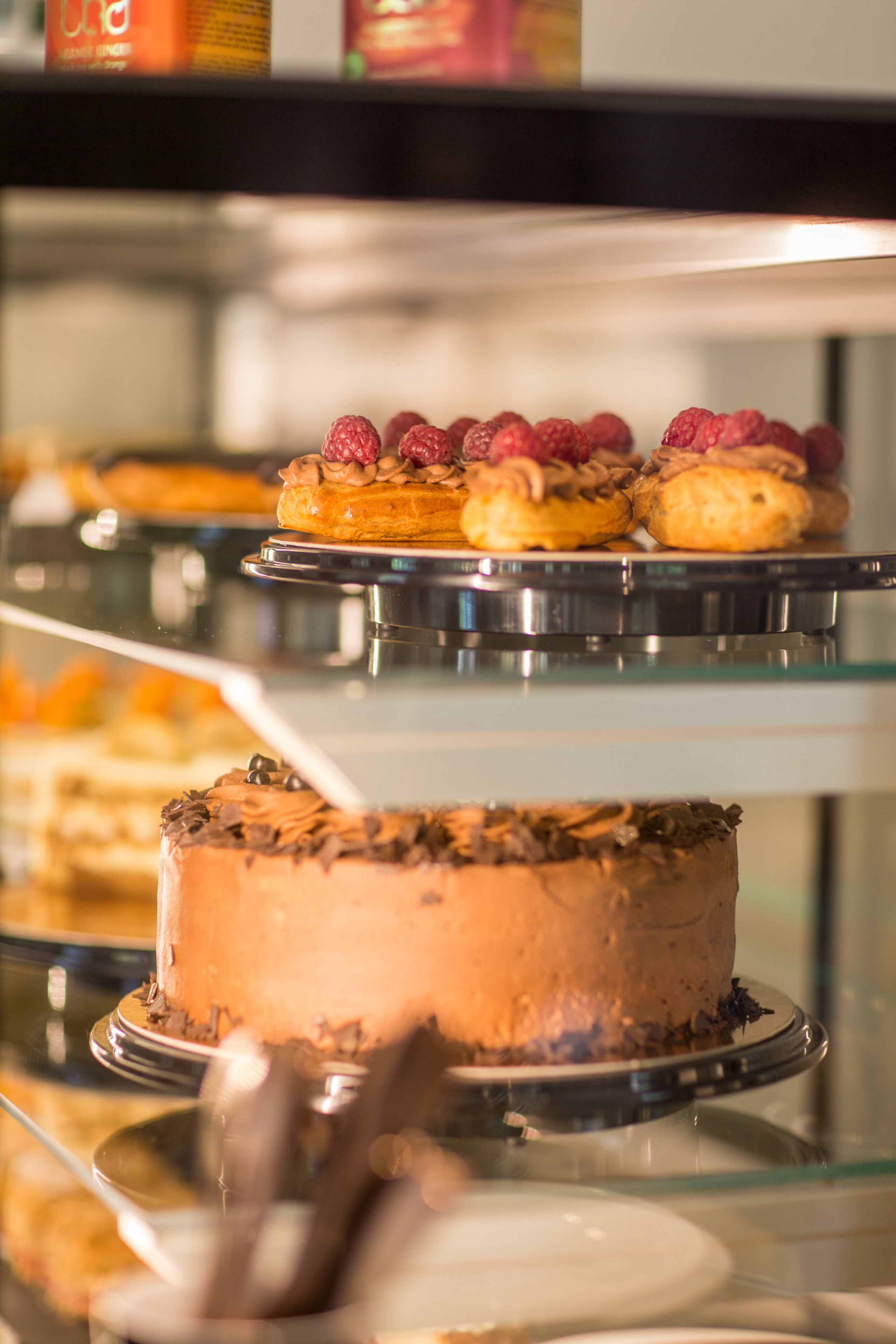 Una vitrina con varios pasteles y postres, incluyendo un pastel de chocolate con frambuesas por encima.