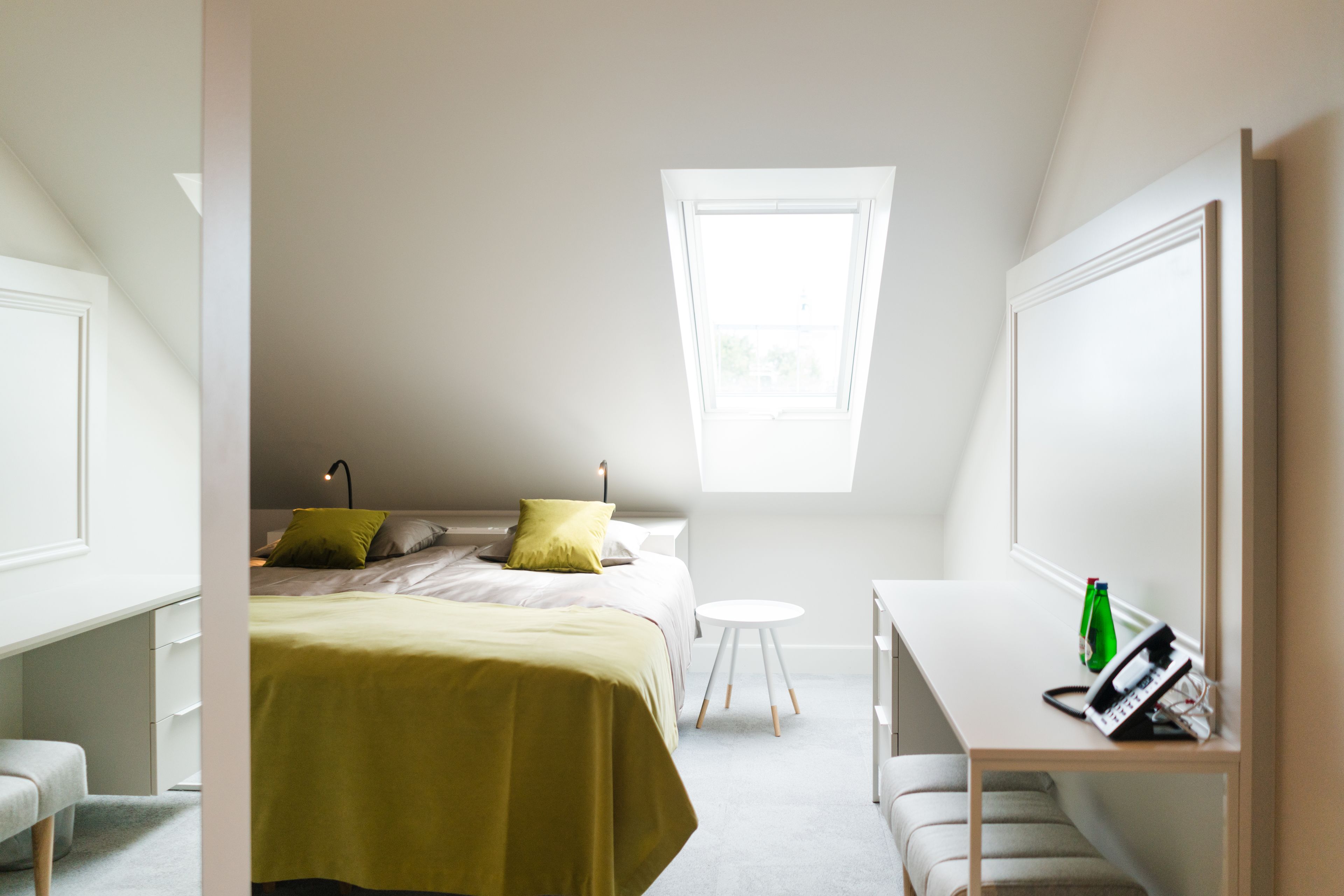 Un dormitorio con cama, escritorio, silla, una mesita y una ventana.