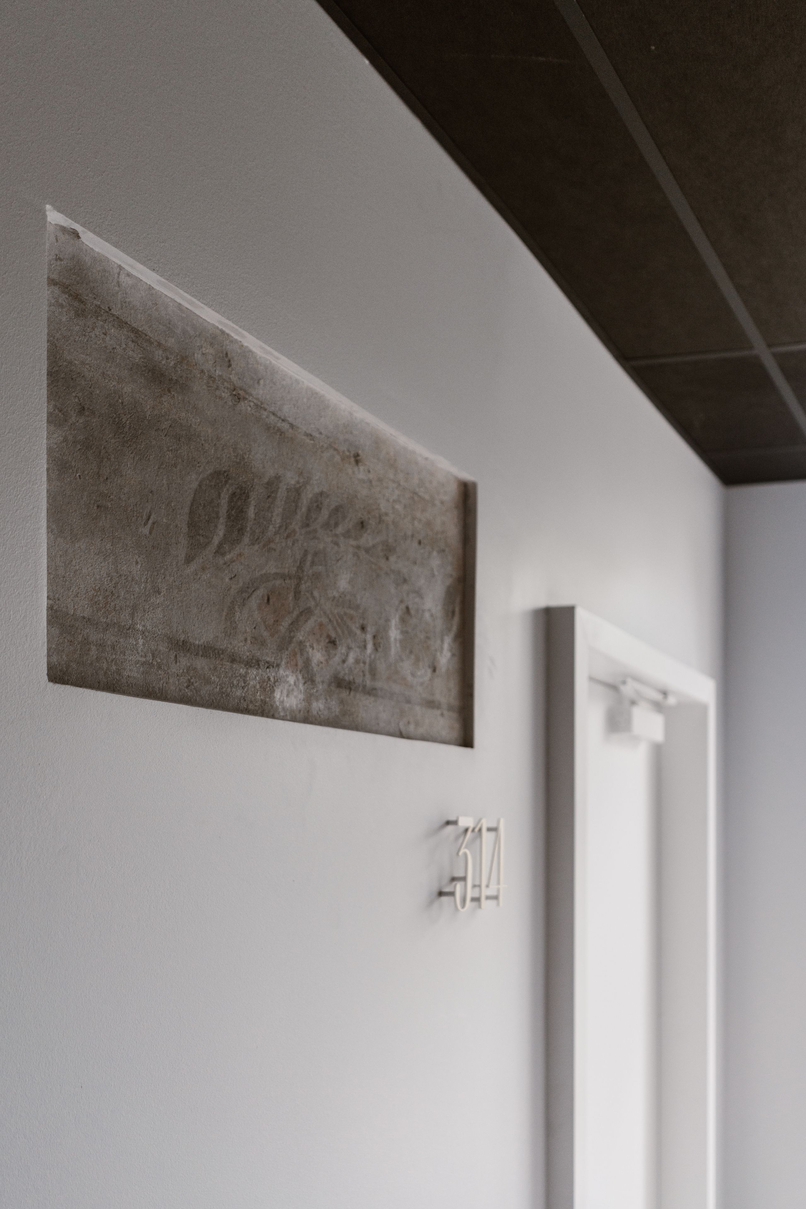 A wall with a textured artwork and a white door with a number plate.