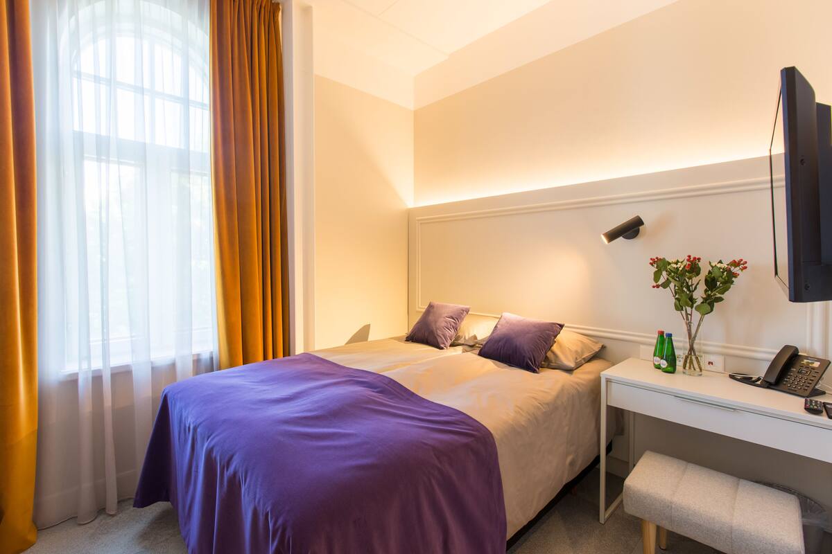 Une chambre d’hôtel avec un lit, un bureau, une chaise, une télévision et une fenêtre avec des rideaux.