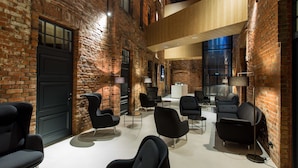 Un vaste espace de détente avec des fauteuils noirs modernes, un mur en briques et un plafond en bois.