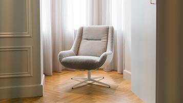 Una habitación moderna con un sillón de color claro, suelo de madera y un ventanal con cortinas translúcidas.