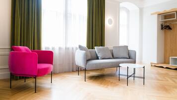 Una sala de estar moderna con un piso de madera clara, un sillón rosa, un sofá gris con cojines estampados y una pequeña mesa blanca.