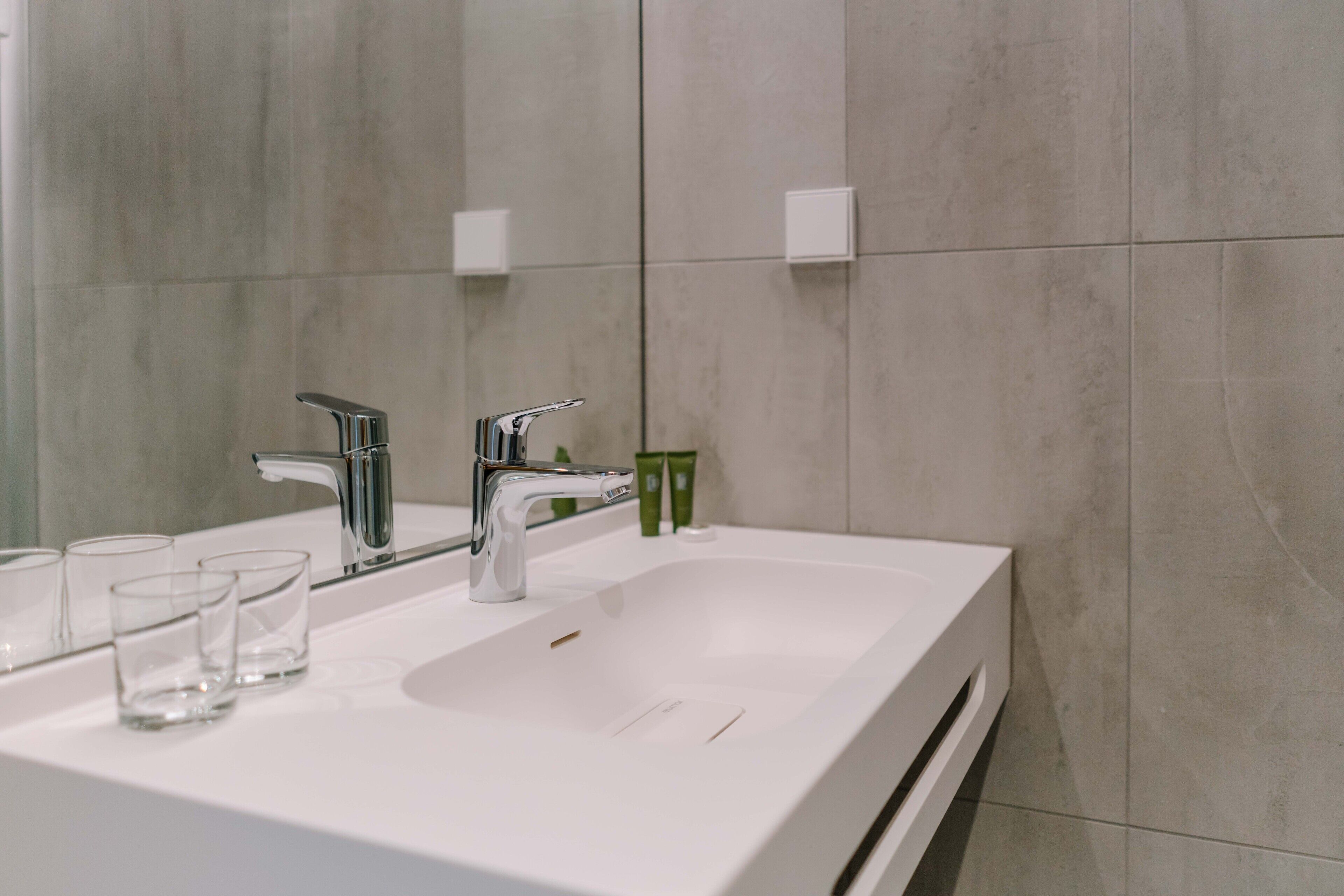 Ein modernes Badezimmer mit einem weißen Waschbecken, zwei Wasserhähnen und einem großen Spiegel.