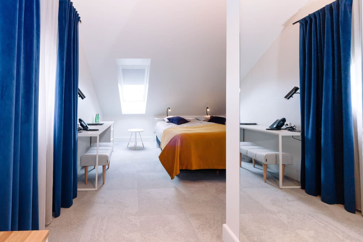 Une chambre à coucher moderne avec un lit, un bureau et une chaise, une petite fenêtre et des rideaux bleus.
