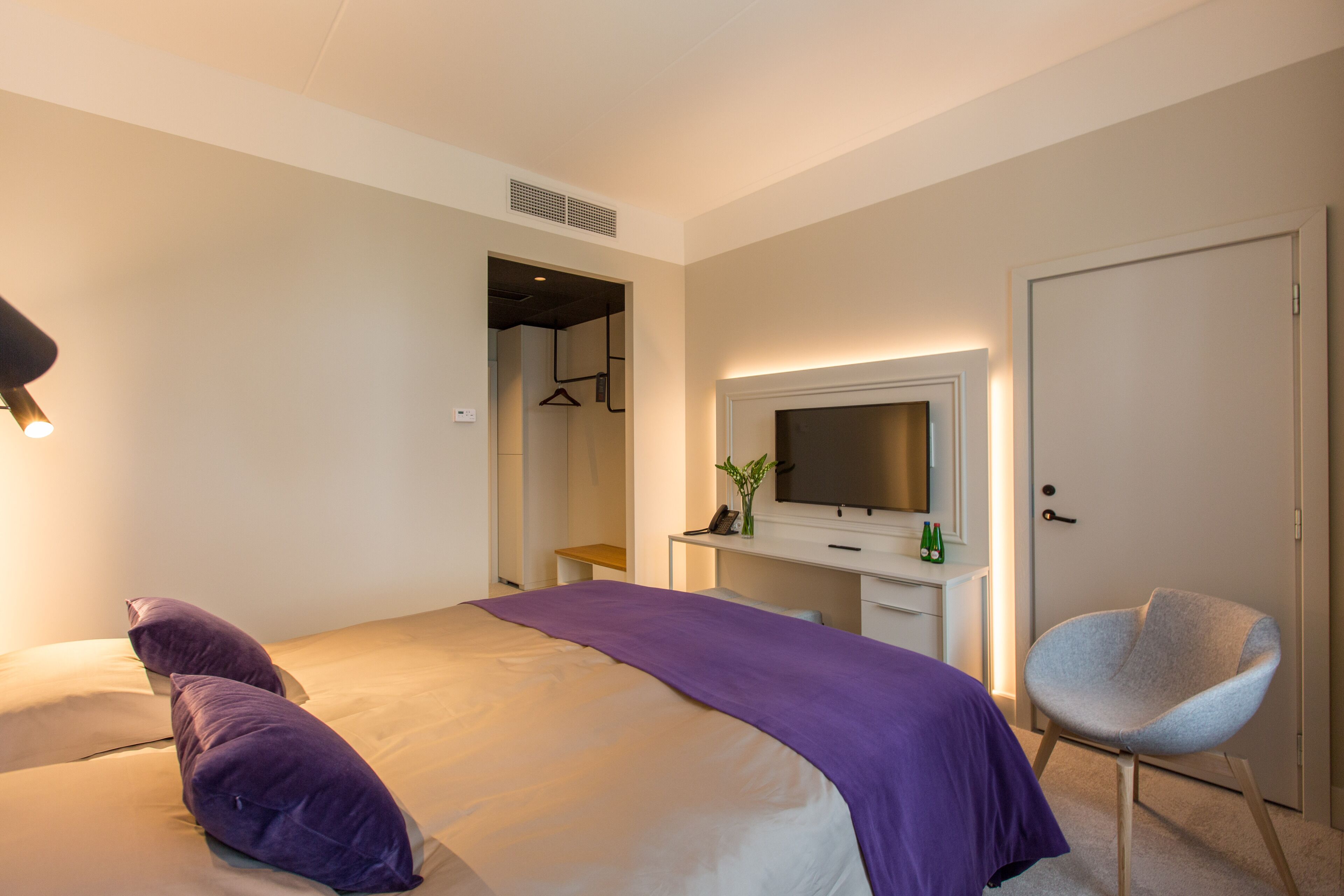 Ein modernes Hotelzimmer mit Bett, Schreibtisch, Stuhl und Fernseher.