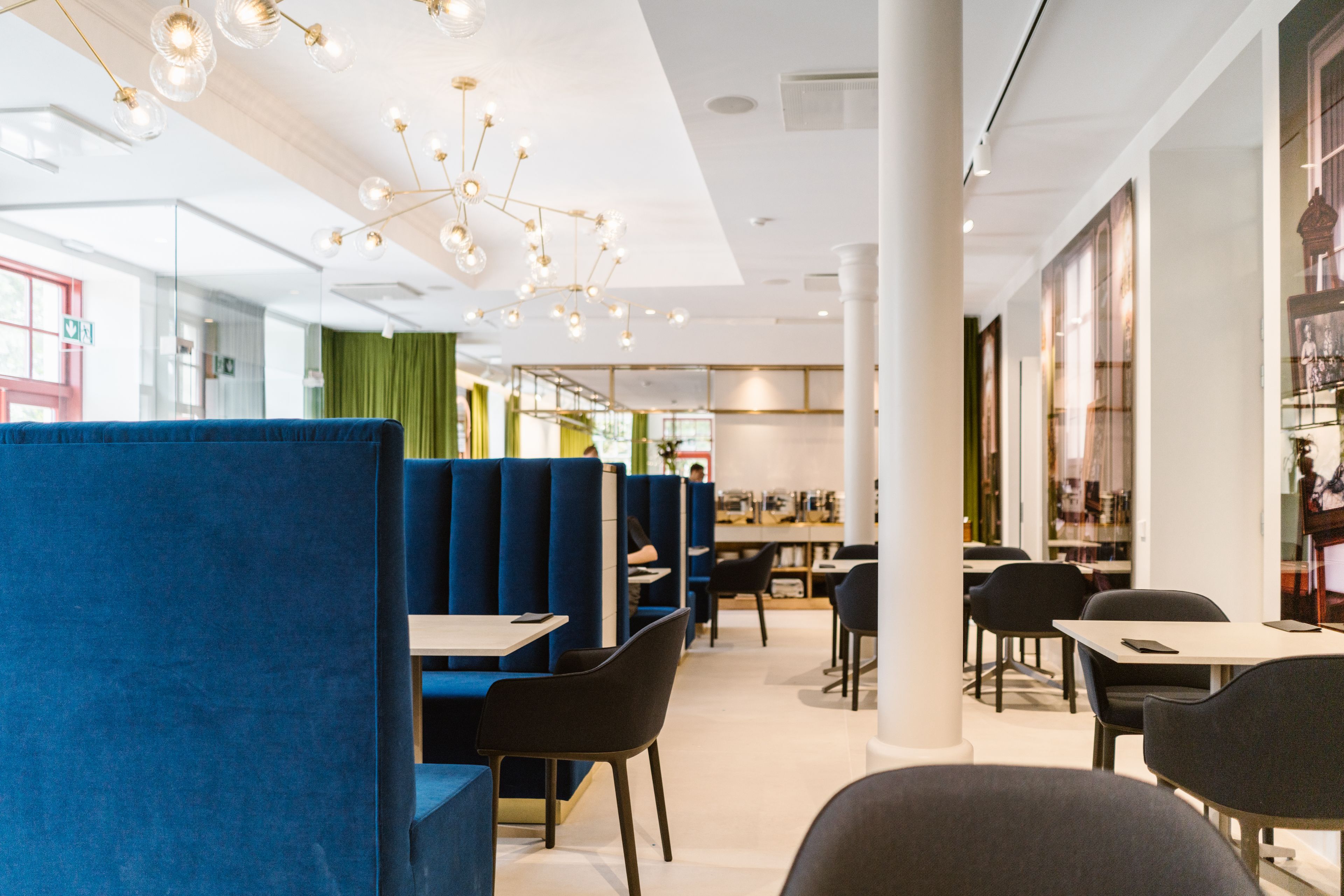 A modern restaurant interior with blue booths, black chairs, and a chandelier.