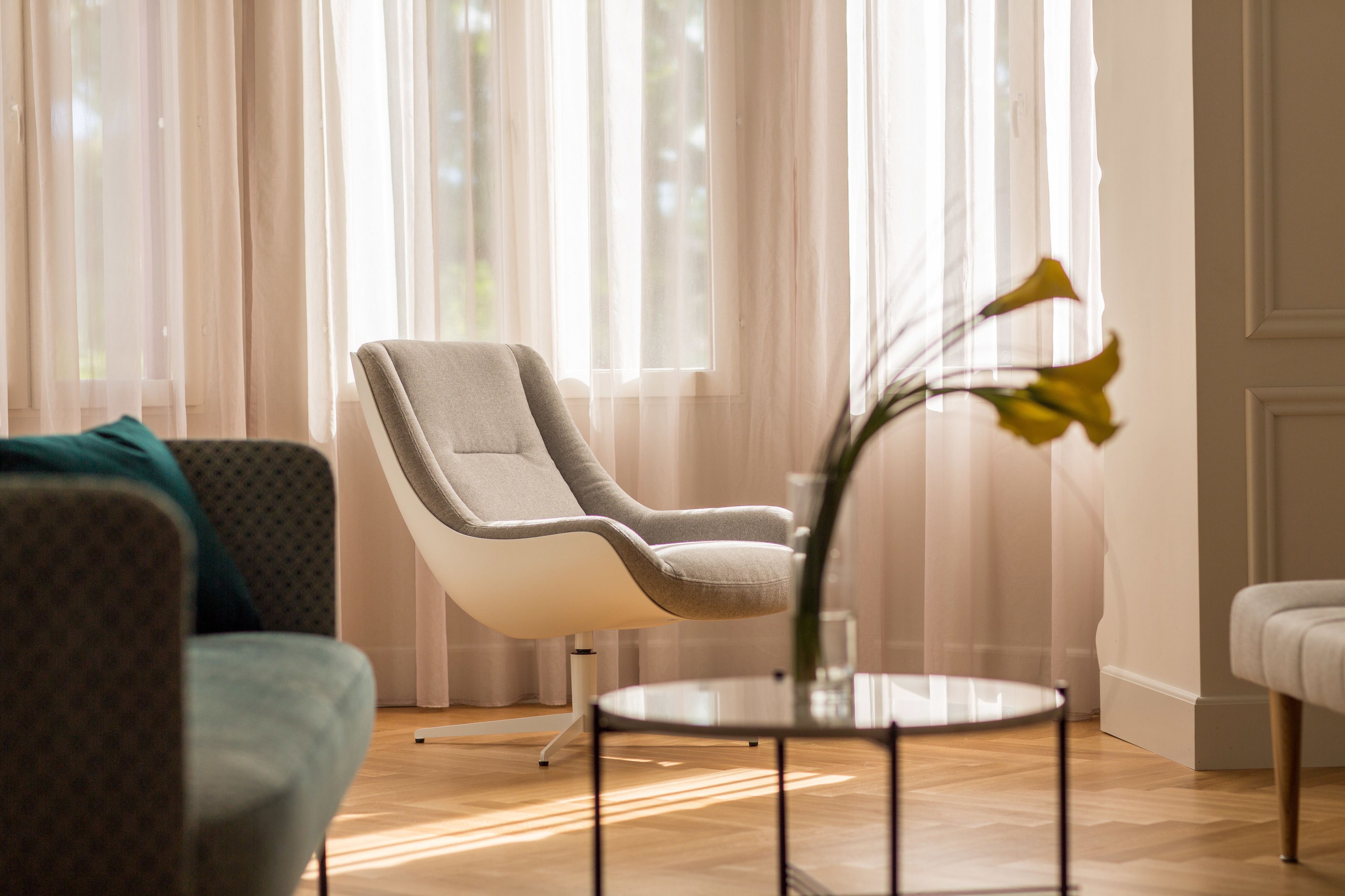 Un salon moderne avec un fauteuil gris, une table basse ronde en verre et un vase rempli de fleurs jaunes.