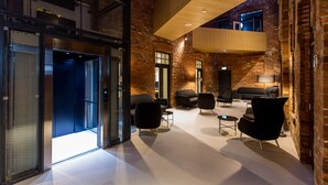 Un hall d’entrée moderne avec un plafond haut, des murs en briques apparentes et un mobilier contemporain.