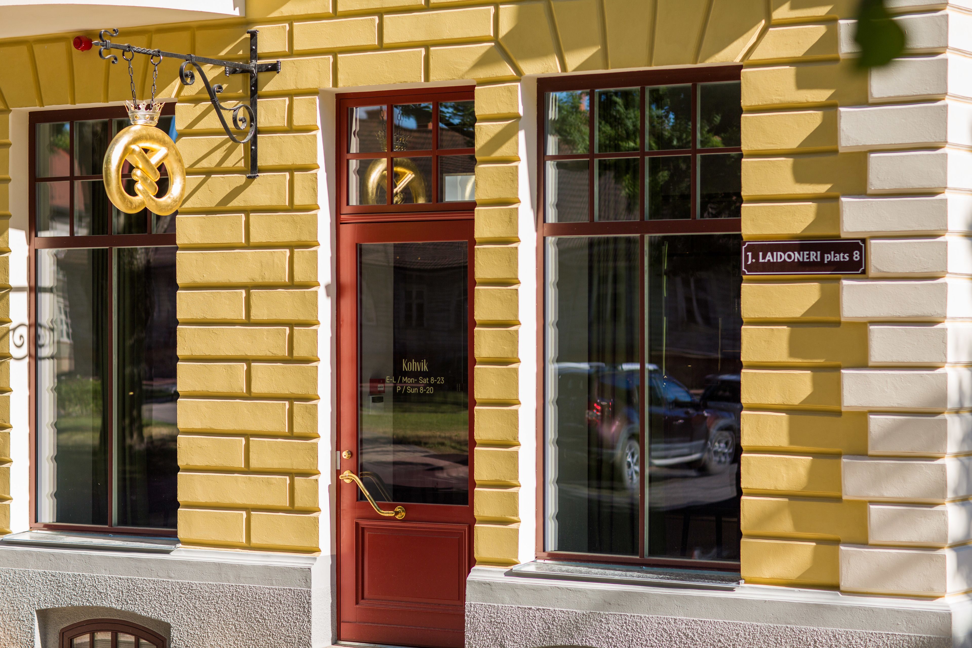 A yellow building with a red door and large windows. A sign on the building reads "J. Laidoneri plats 8".