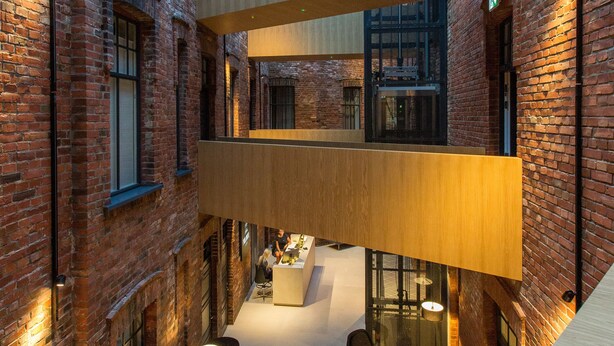 Un vaste atrium doté de hauts plafonds, de murs en briques apparentes et d’un espace de détente central aménagé avec des meubles modernes.