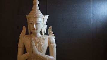 Eine Statue mit aufwendigen Schnitzereien und einer spitz zulaufenden Spitze vor dunklem Fliesenwerk.