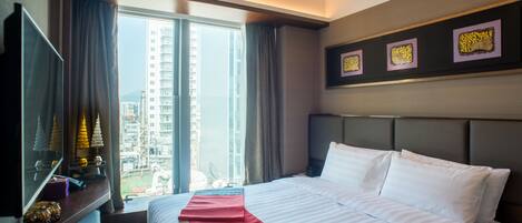 A hotel room with a large bed, a desk with a computer, and a window with a city view.