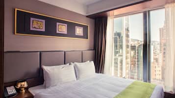A hotel room with a large bed, a nightstand with a phone, and a window with a city view.