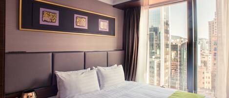 Habitación de hotel con una cama grande, una mesita de noche con teléfono y una ventana con vista a la ciudad.
