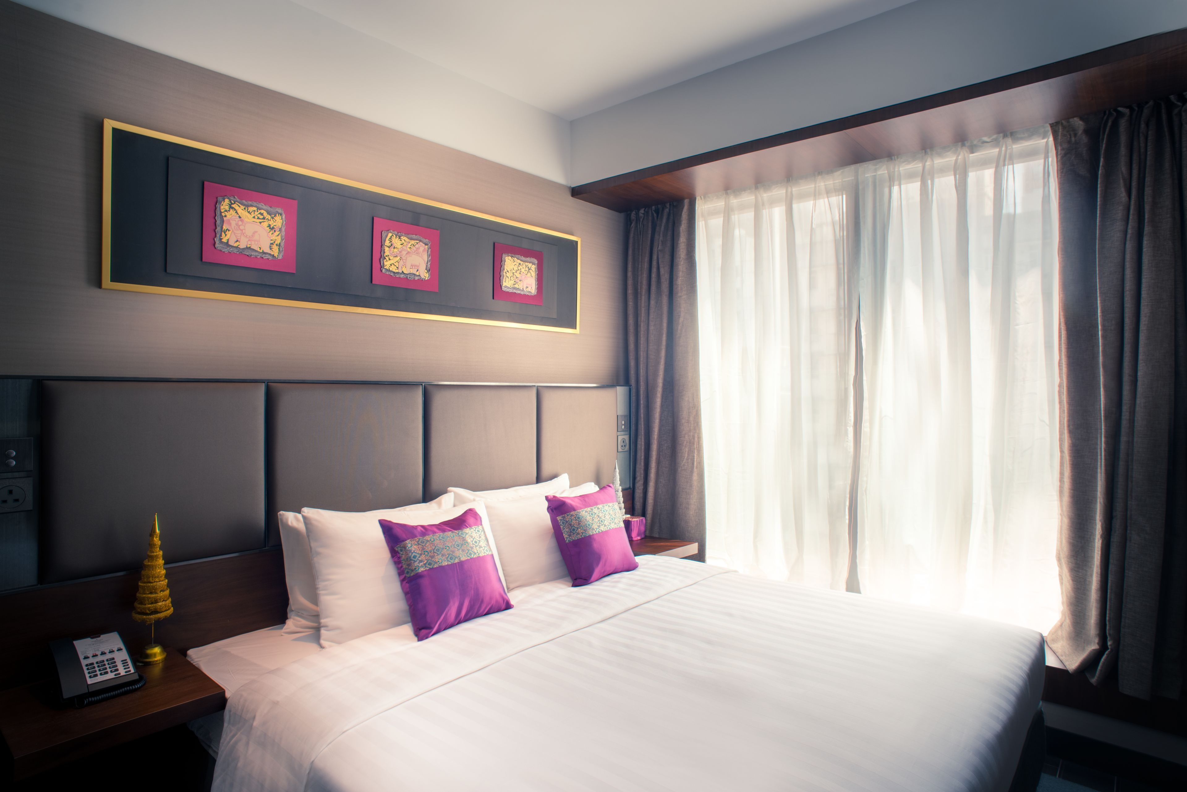 Een hotelkamer met een groot bed, twee kussens, een nachtkastje met een lamp en een telefoon aan de muur.