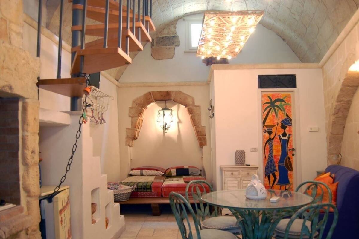 A cozy room with a stone wall, a bed with a colorful quilt, a dining table with chairs, and a painting on the wall.