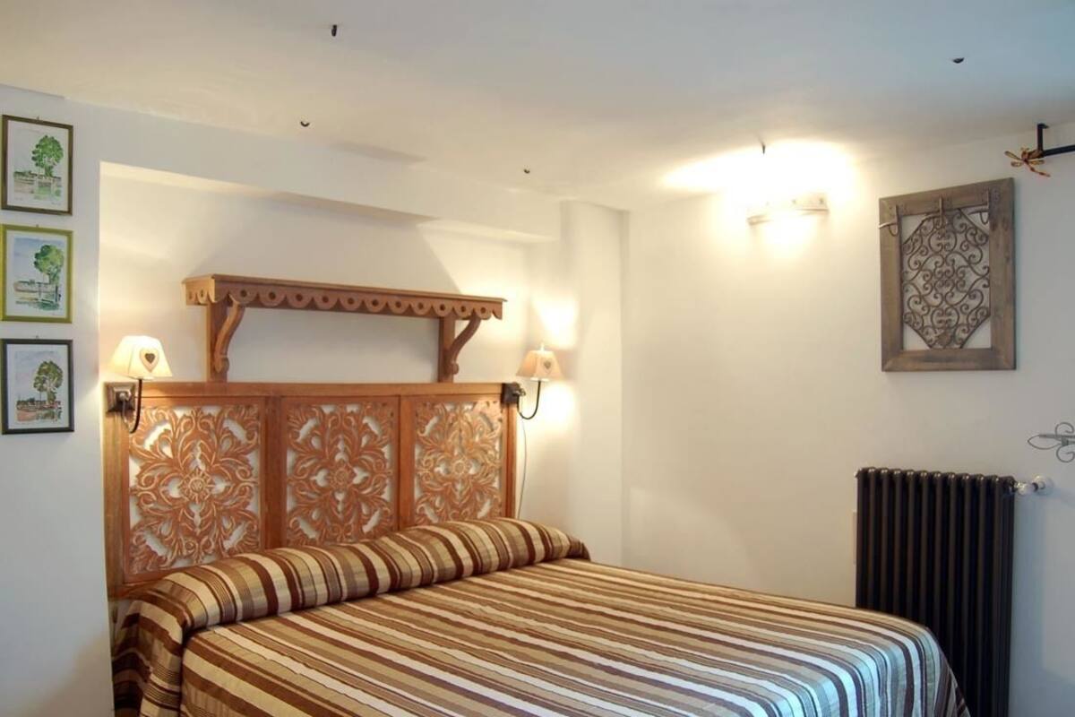 A bedroom with a wooden headboard, a bed with striped bedding, wall-mounted lamps, and a radiator.