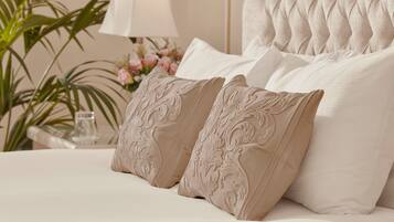 A bed with two decorative pillows, a bedside table with a glass, and a potted plant.