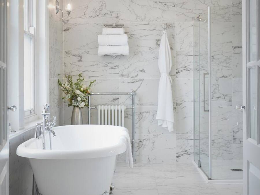 A bathroom with a freestanding bathtub, a glass shower enclosure, marble walls, and a chandelier.