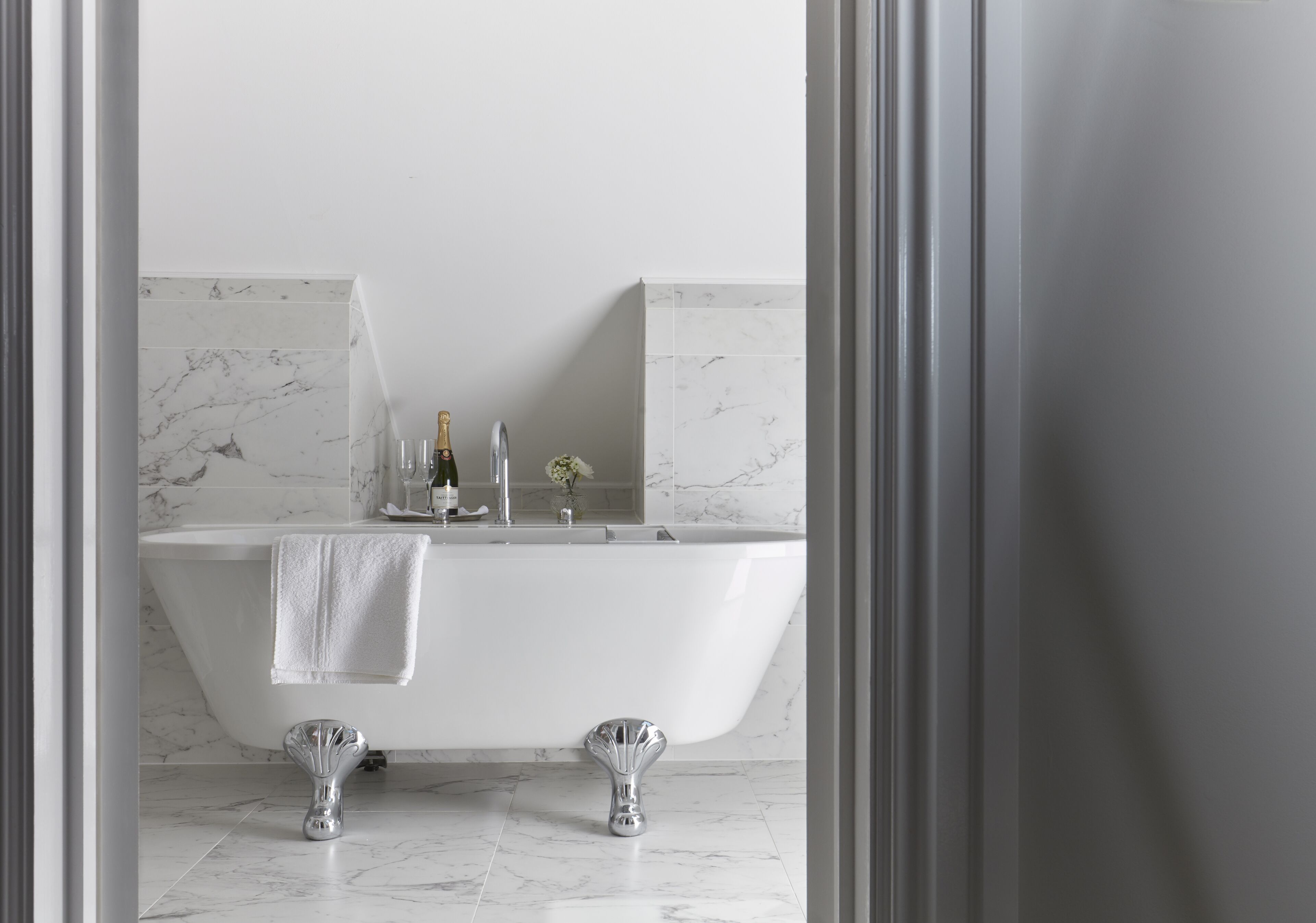 A modern bathroom with a freestanding bathtub, marble tiles, and a champagne bottle on the counter.