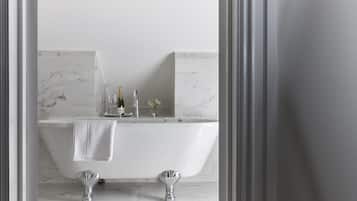 A modern bathroom with a freestanding bathtub, marble tiles, and a champagne bottle on the counter.