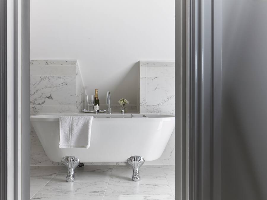 A modern bathroom with a freestanding bathtub, marble tiles, and a champagne bottle on the counter.