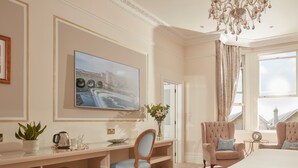 A hotel room with a large bed, a desk with a chair, a television, and a view of the city through the window.