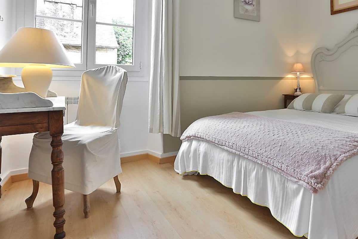Ein ordentlich eingerichtetes Schlafzimmer mit einem Bett, Nachttischen, einem Sessel und einem Fenster.