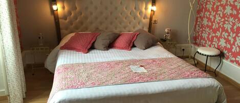A bedroom with a large bed, a bedside table, a nightstand, a small stool, and a wall with a floral pattern.