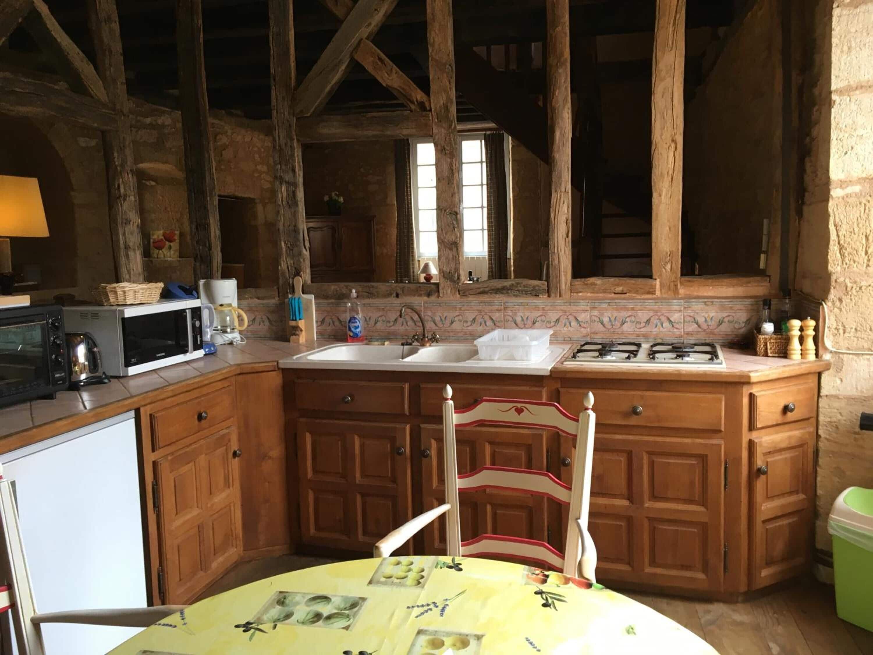 A rustic kitchen with wooden beams, a sink, a stove, and a table with a yellow tablecloth.