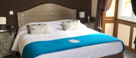 Een netjes opgemaakt bed met een blauw-bruine plaid, een houten hoofdbord en een nachtkastje met een lamp.