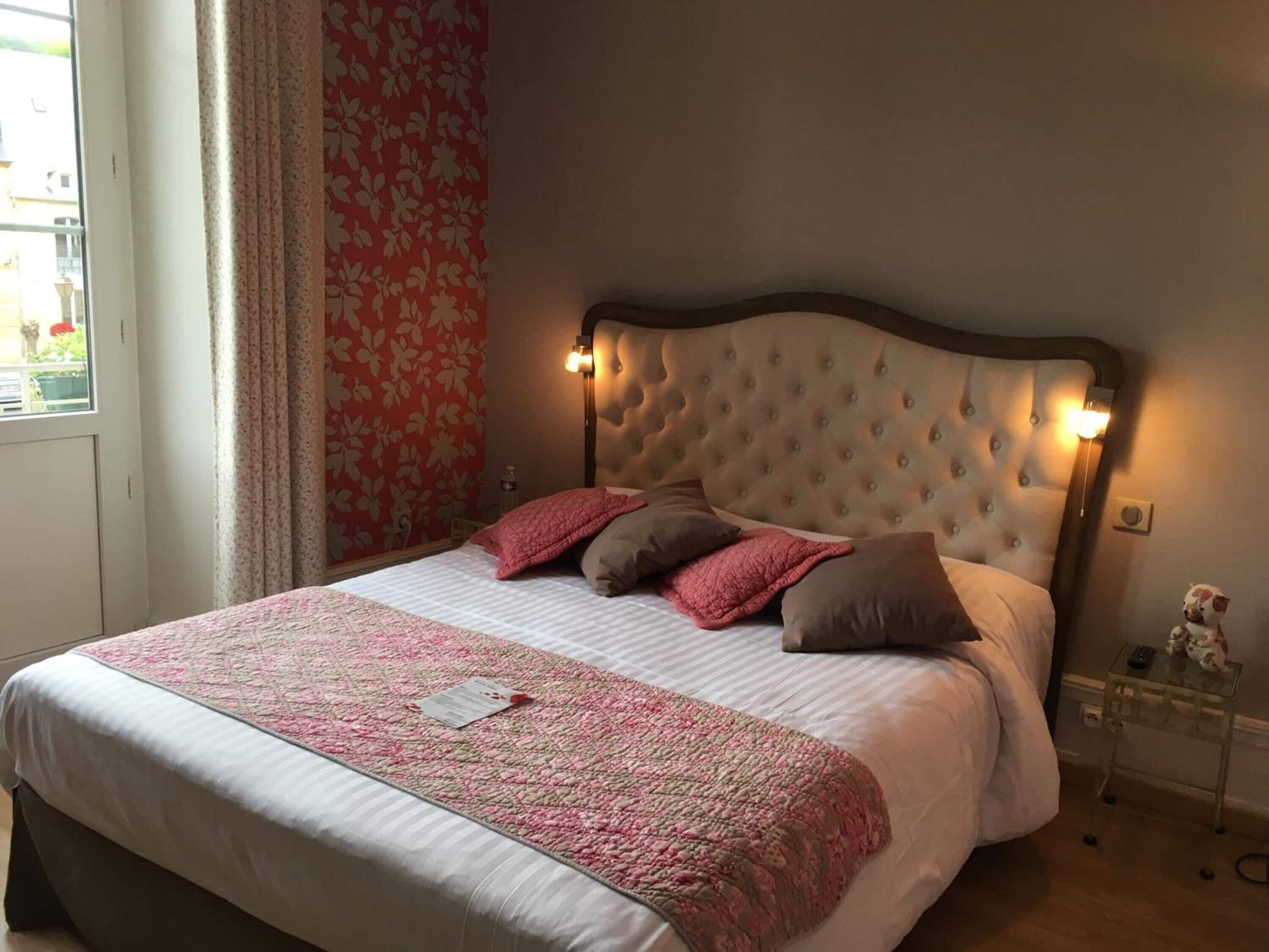 Un dormitorio con cabecera capitonada, cama con ropa de cama rosa y blanca, y una mesita de noche con un osito de peluche.