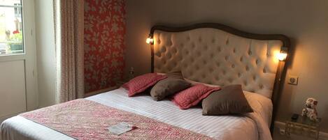 Un dormitorio con cabecera capitonada, cama con ropa de cama rosa y blanca, y una mesita de noche con un osito de peluche.