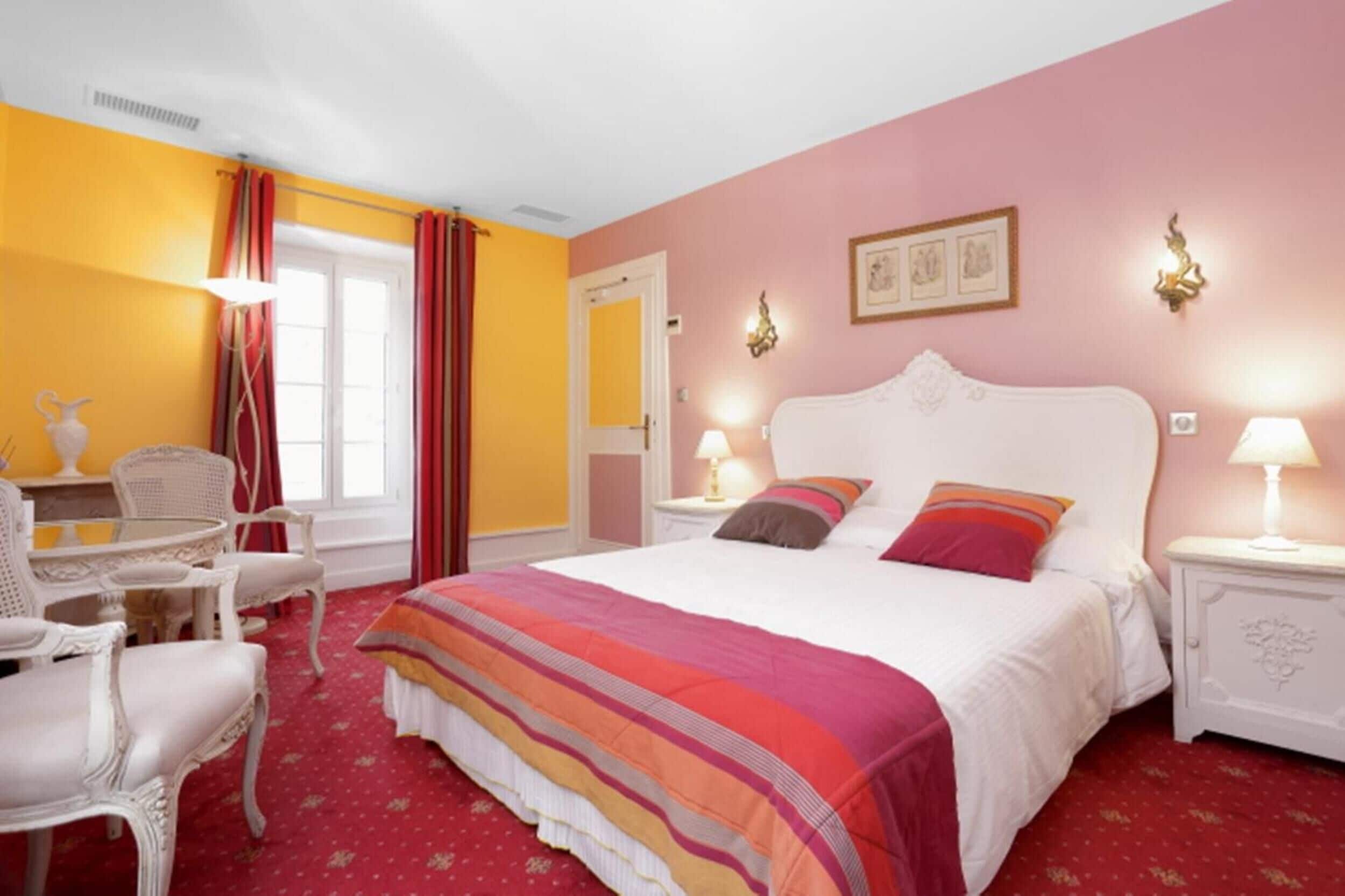 A hotel room with a large bed, a dining table with chairs, and a window with curtains.