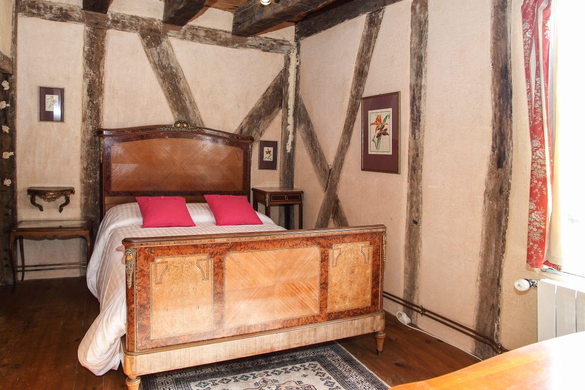 A traditional bedroom with a wooden four-poster bed, a nightstand, and a red curtain.