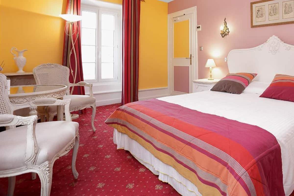 Ein Schlafzimmer mit einem großen Bett, zwei Nachttischen, einem Sessel und einem kleinen Tisch.