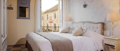 A bedroom with a large bed, a nightstand, a dresser, and a window overlooking a building.