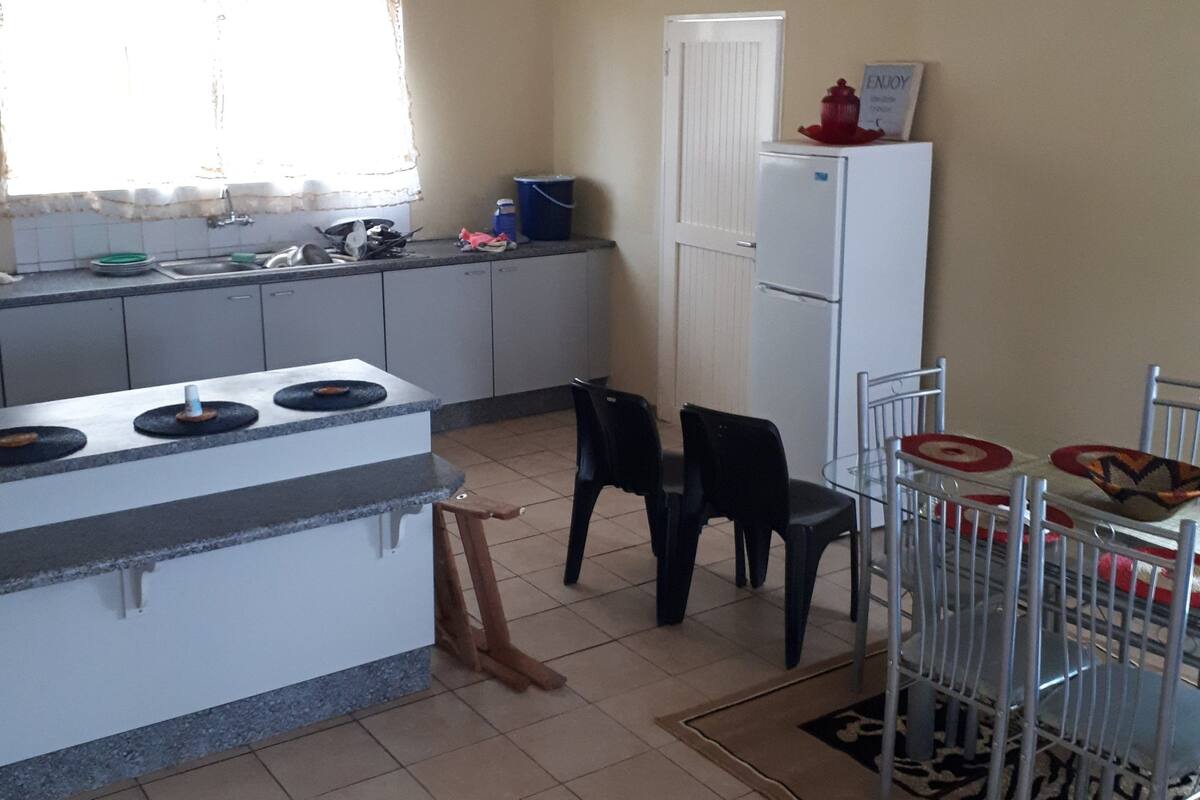 Una cocina con mostrador, pileta y heladera. Hay sillas y una mesa de comedor.