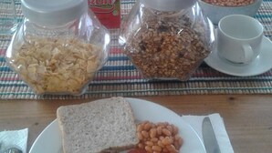Una mesa de desayuno con tostadas, salchichas, huevos, frijoles y un cartón de jugo de frutas.