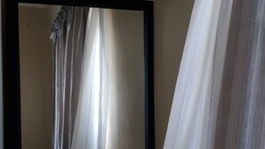 Una habitación con un espejo grande en la pared, una cortina entreabierta y una pared lisa.